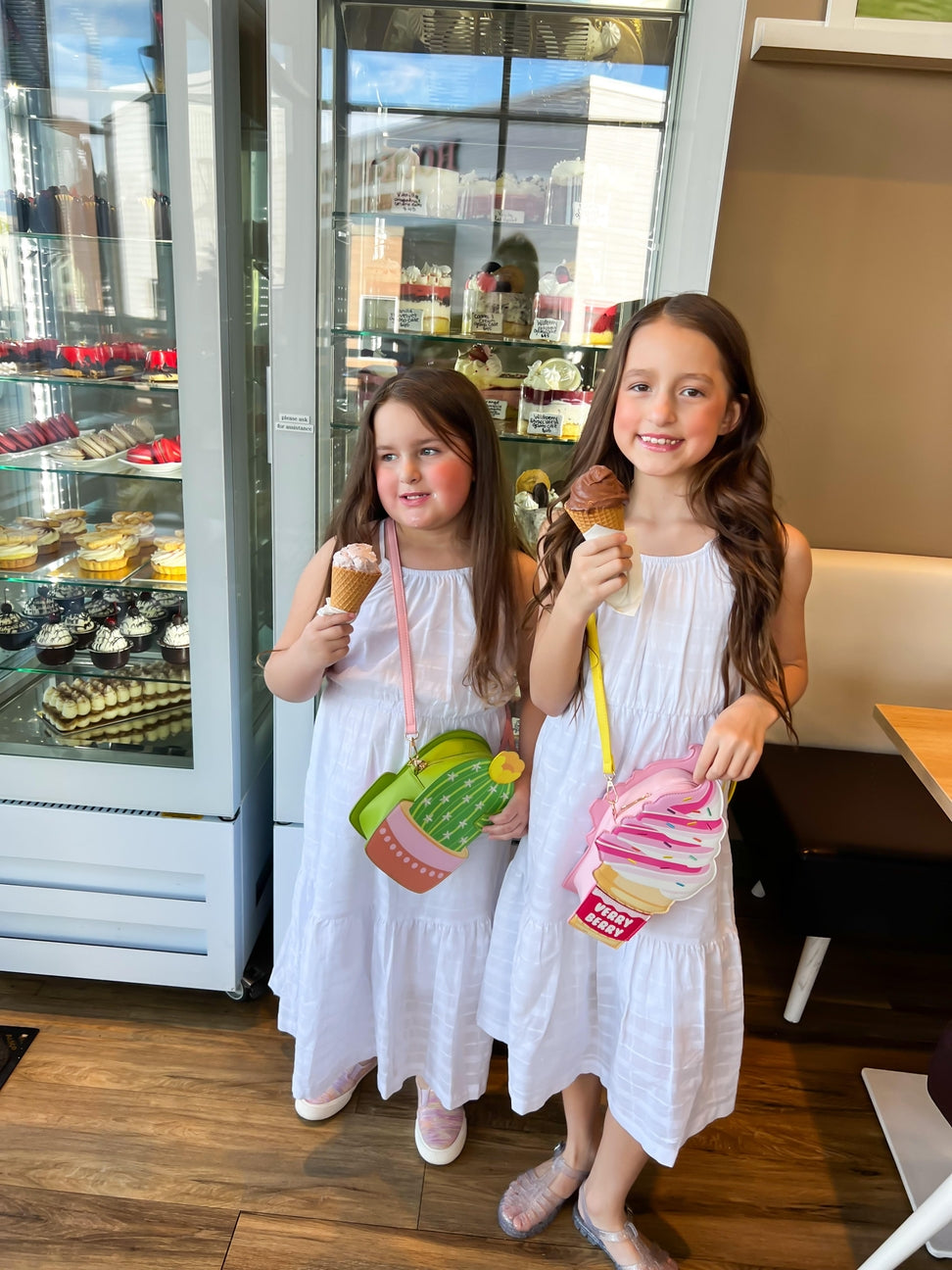 Two young girls in white dresses holding ice cream cones in a dessert shop.