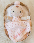 Knitted baby doll with a blanket in a basket on a soft beige background