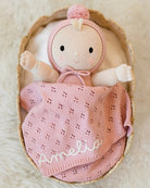 Baby doll in a pink outfit with 'Amelia' embroidered on it, wrapped in a matching blanket inside a wooden basket.