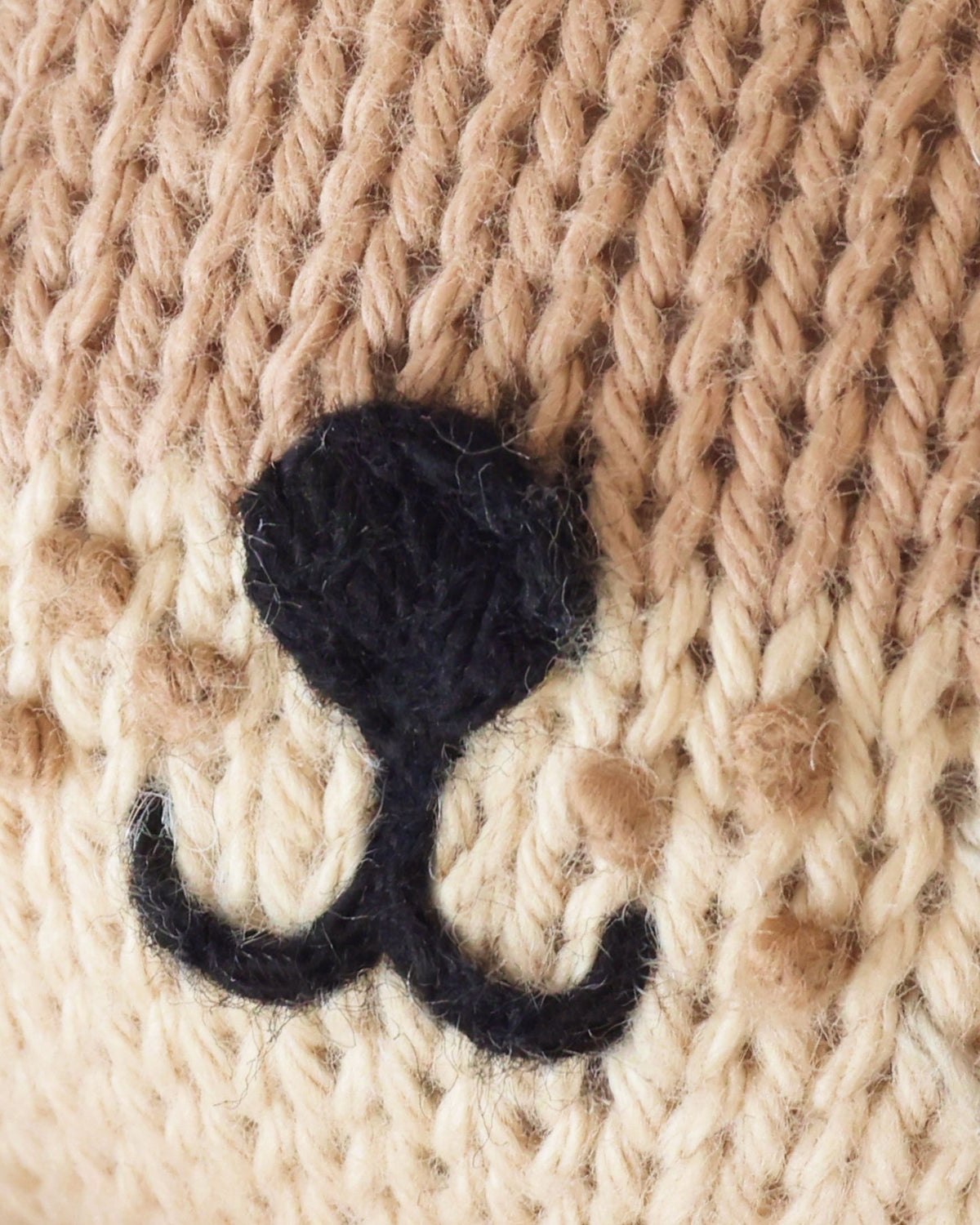Close-up of a beige knitted mitten with black embroidered nose, and mouth.