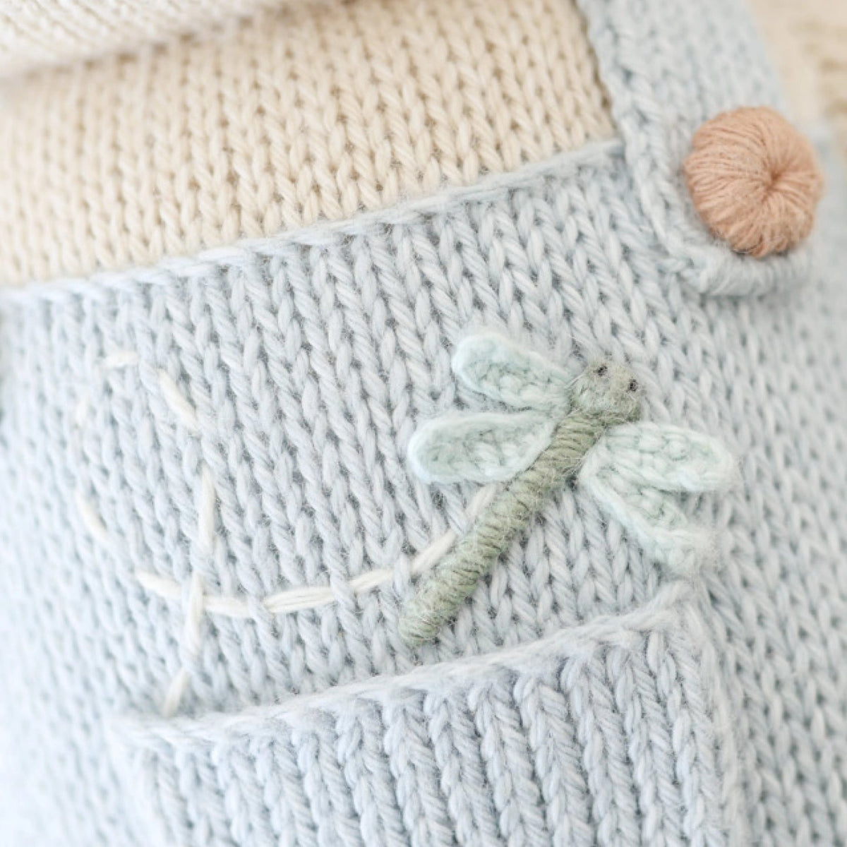 Close-up of a knitted fabric with a dragonfly design and a yarn ball.
