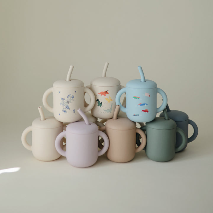 Collection of colorful ceramic cups with lids and straws on a light background