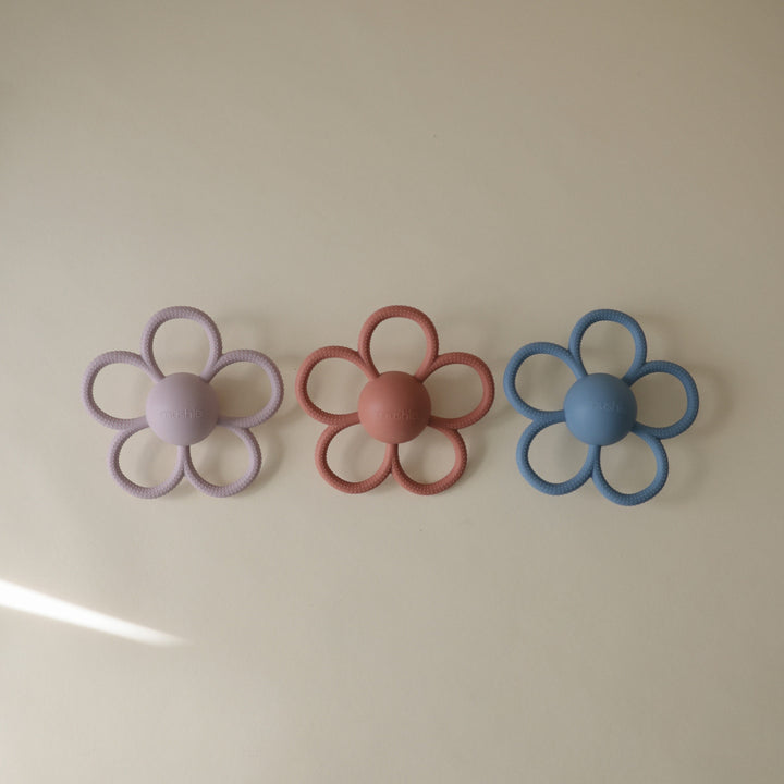 Three flower-shaped objects in purple, pink, and blue on a plain background