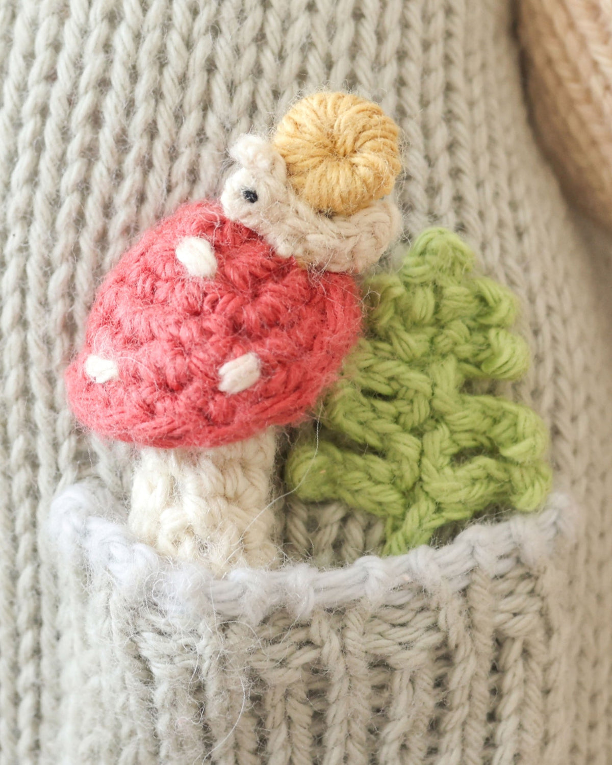 Knitted mouse on a red mushroom with a green leaf against a textured beige background