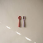 Two baby rattles, one red and one purple, on a beige surface.