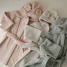 Pink, beige, and gray bathrobes with matching hats on a neutral background
