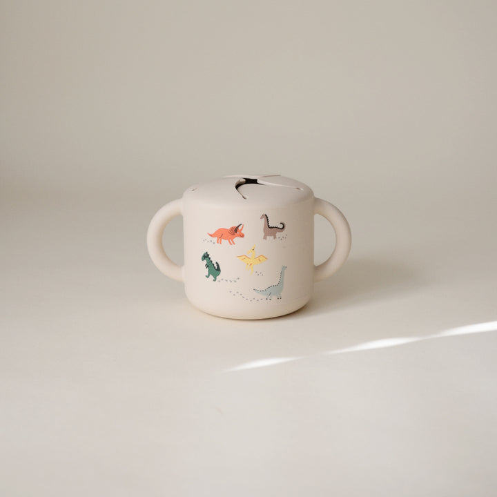 White children's cup with dinosaur illustrations on a beige background