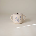 White ceramic mug with blue floral patterns on a light beige background