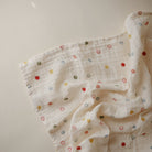 Folded white muslin baby swaddle blanket with a colorful smiley face pattern.