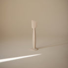 A minimalist, matte off-white silicone spatula standing upright on a matching circular base against a solid beige background.