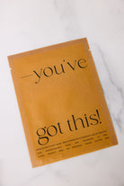 Product packaging with text 'you've got this!' on a white marble surface