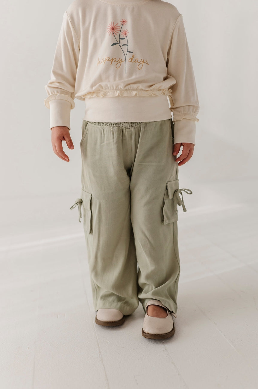 Person wearing a beige sweatshirt with floral design and text, paired with green cargo pants on a white background