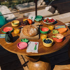 Wooden table with colorful plates, bowls, and food items outdoors.