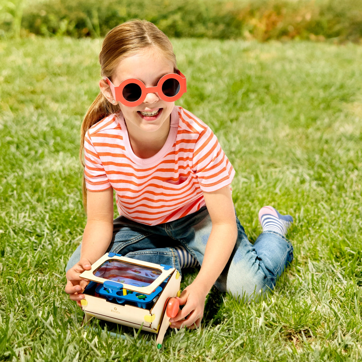 Child wearing red sunglasses sitting on grass with a toy solar car