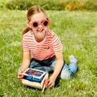 Child wearing red sunglasses sitting on grass with a toy solar car
