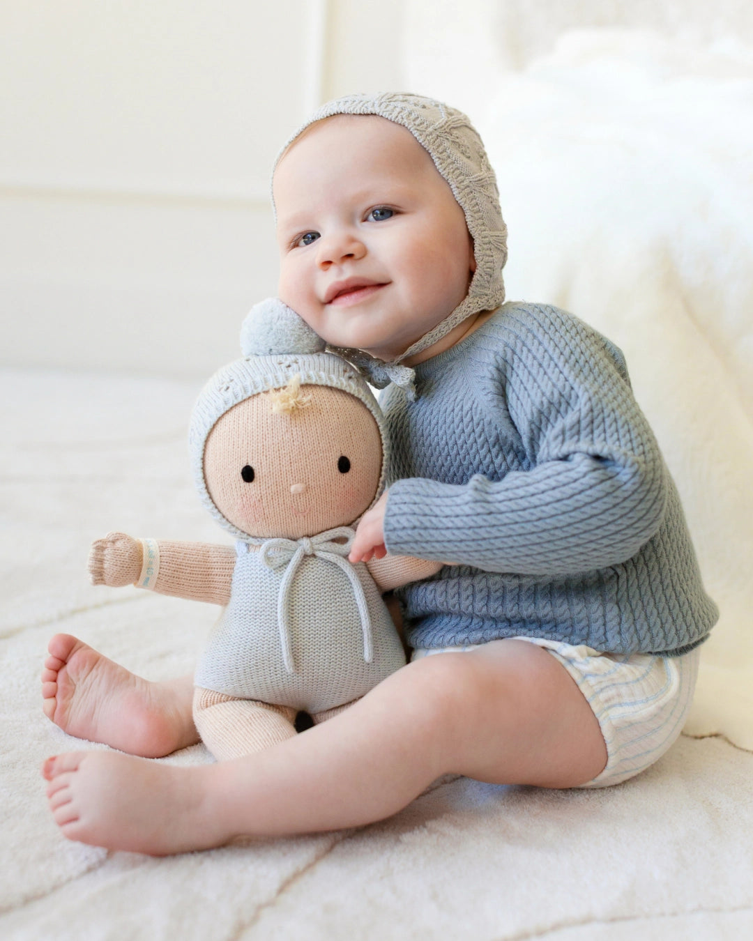 Baby in blue outfit holding a soft toy on a white background