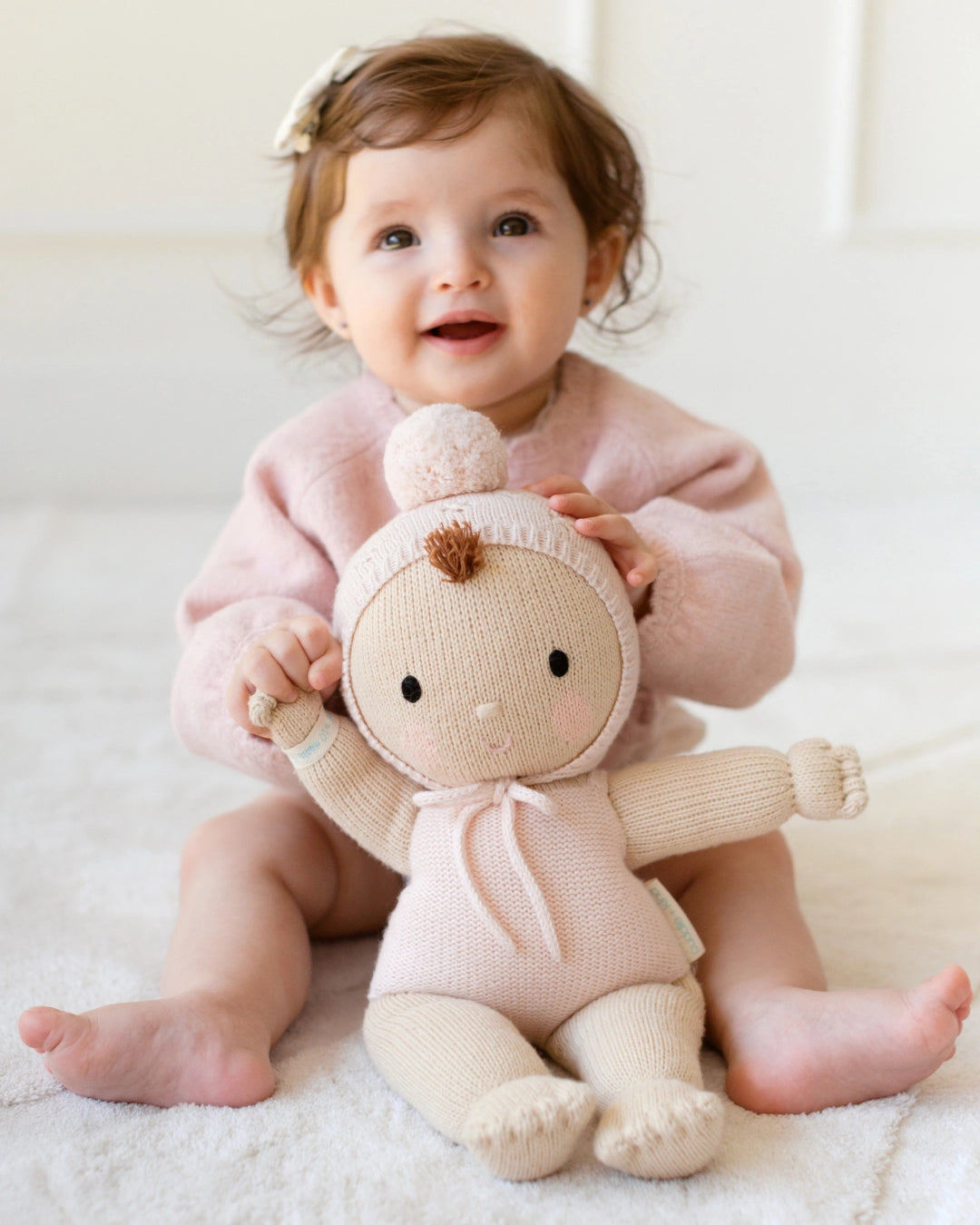 Baby in pink outfit holding a plush toy with a white background
