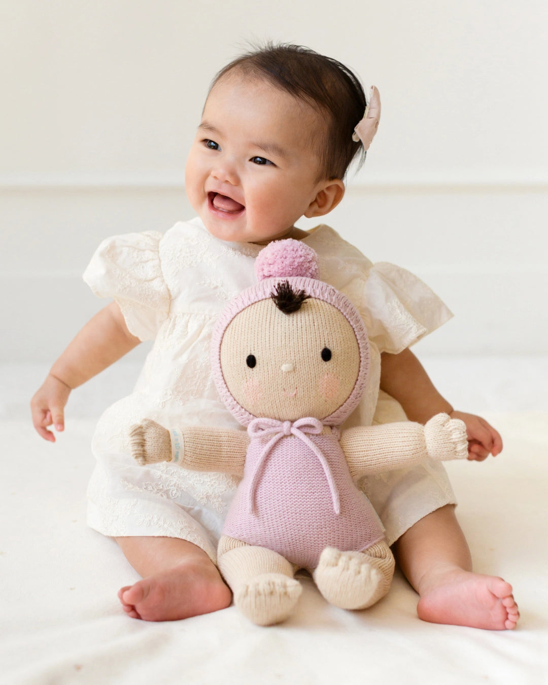 Baby holding a knitted doll with a pink outfit on a white background