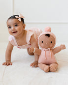 Baby crawling next to a knitted doll wearing a pink outfit on a white background
