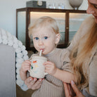 Child drinking from a cup held by an adult in a home setting