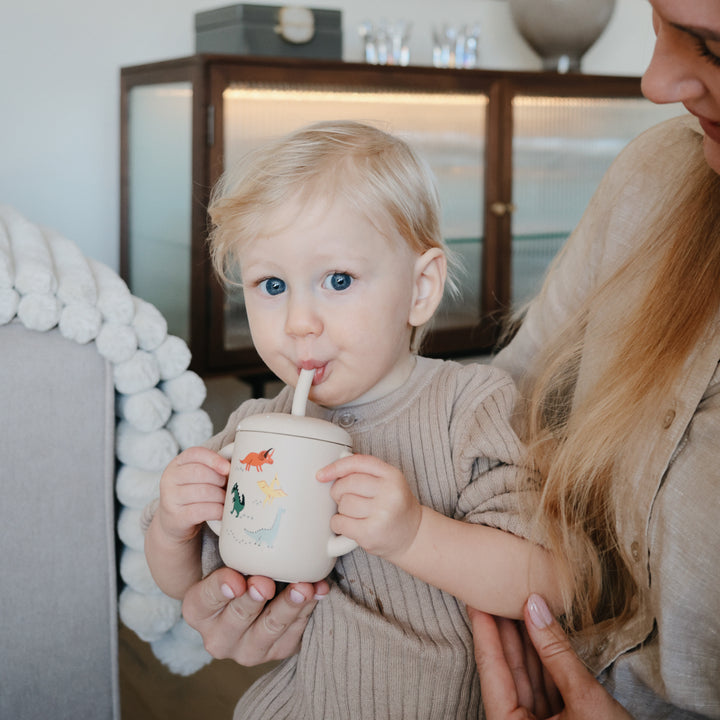 Child drinking from a cup held by an adult in a home setting