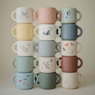 Stack of colorful children's mugs with various designs on a neutral background