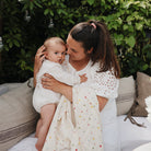 A woman holding a baby wrapped in a white smiley-face muslin swaddle blanket on an outdoor couch.