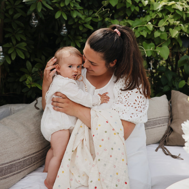 A woman holding a baby wrapped in a white smiley-face muslin swaddle blanket on an outdoor couch.