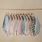 Row of baby rompers on hangers against a beige wall