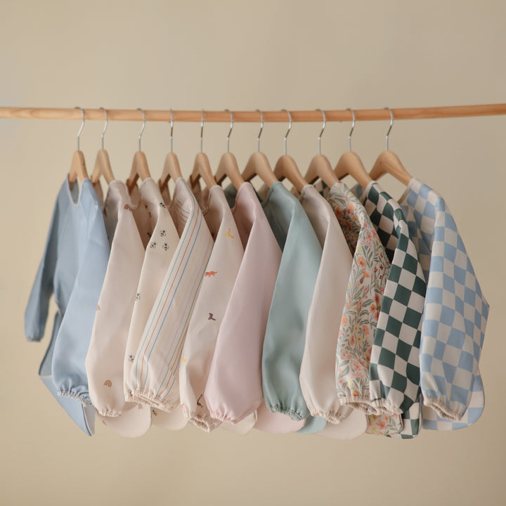 Row of baby rompers on hangers against a beige wall