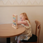 Child playing with an abacus at a table against a neutral wall.