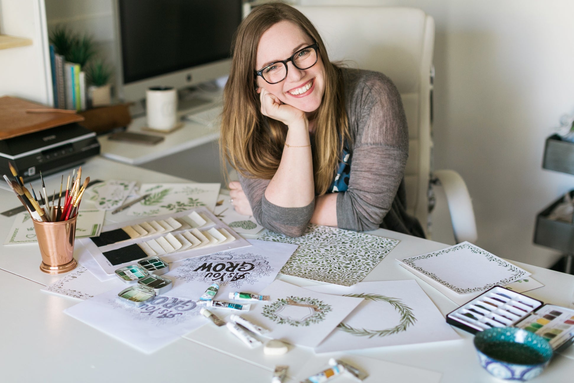 Woman sitting at a desk with design materials and a computer in the background