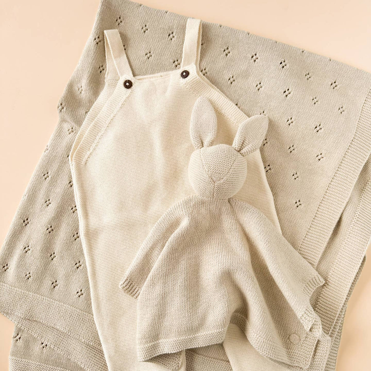Beige baby romper with bunny ears on a textured beige blanket
