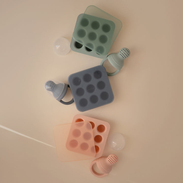 Colorful silicone ice cube trays with bottles on a beige background