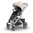 A modern stroller with a beige canopy, black seat and storage basket, and a silver and dark gray frame, shown on a clean white background.
