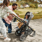 Family with a child in a stroller walking outdoors on a path.