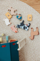 An overhead, bird's-eye view of the Wooden Big Red Barn Playset by Mentari components laid out on a textured surface, including seven wooden animal figures—a cow, horse, pig, sheep, goat, chicken, and rooster—alongside a blue ladder, a small stool, and a piece of fencing.