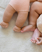 Close-up of a baby's feet and legs next to a knitted doll on a soft surface