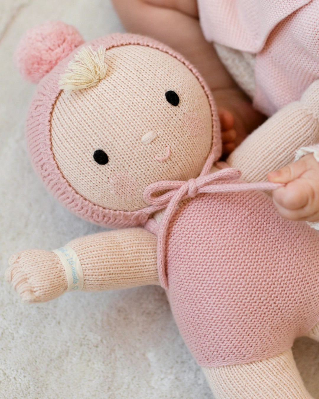 Knitted doll with pink hat and dress held by a person on a light background