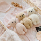 Three small teddy bears on a pink blanket with wooden toys and a heart-shaped object.