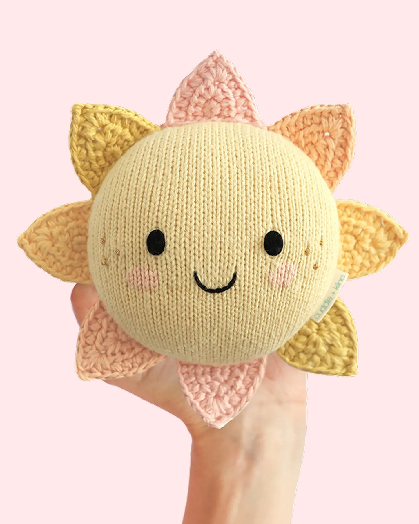 Knitted sunflower plush toy held in a hand against a pink background