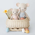 Two knitted mouse toys in a wicker basket with a book and Easter eggs on a light gray background