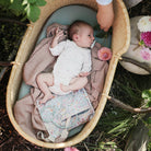 Baby lying in a woven basket with floral decorations outdoors