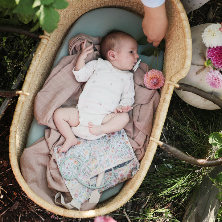 Baby lying in a woven basket with floral decorations outdoors