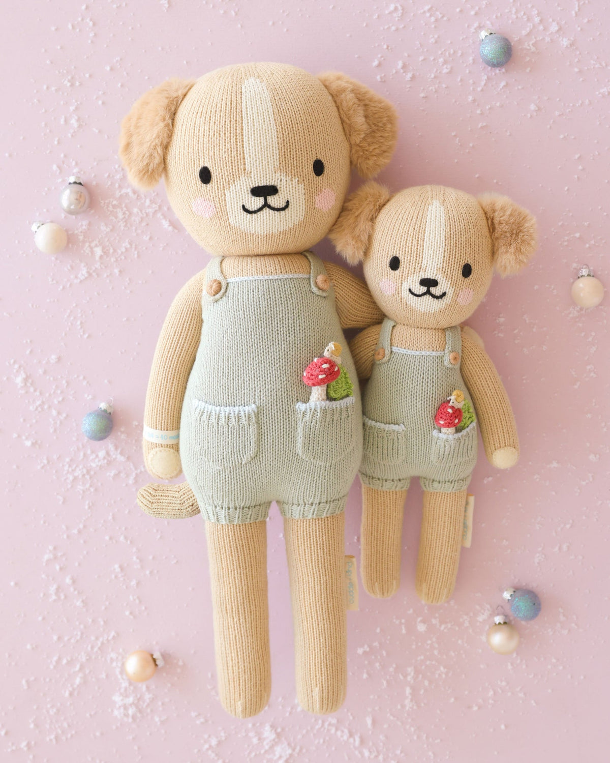 Knitted bear toy with overalls, baby booties, and photo on a textured surface with Christmas decorations.