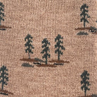 Close-up of a woven fabric with a repeating pattern of dark green pine trees on brown ground over a warm tan background.