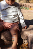 Child sitting on stone steps with temporary tattoos on arms and legs, outdoors.