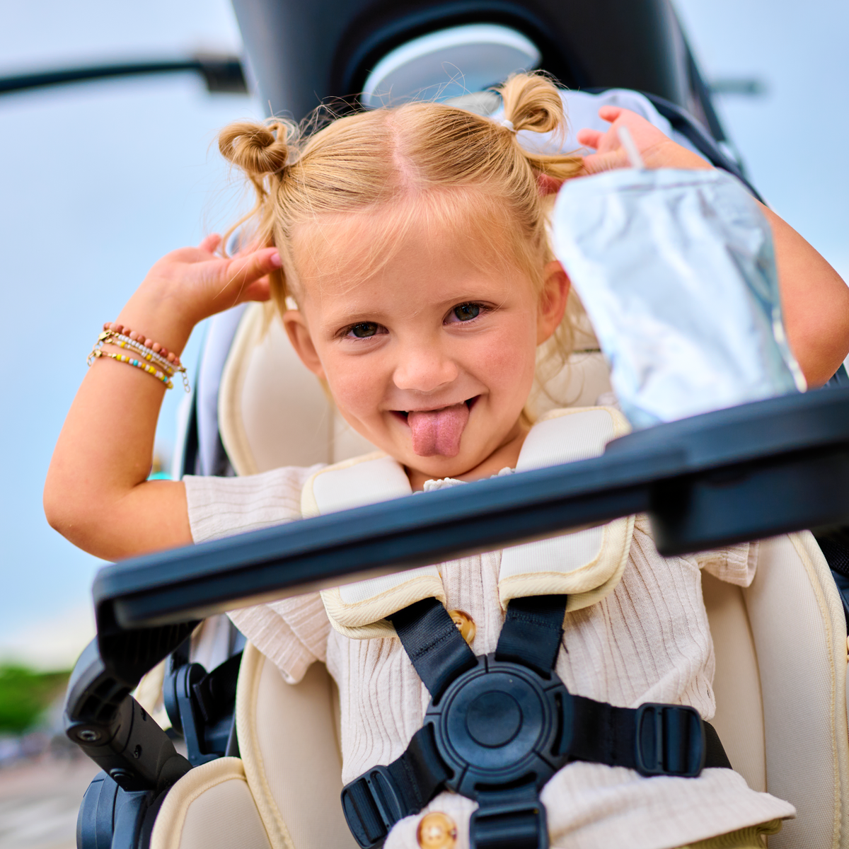 Child in a stroller sticking out tongue with a clear blue sky background