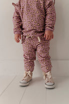 A toddler standing in a matching dusty pink leopard-print pajama set with beige sneakers, photographed against a clean white studio background.
