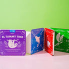 Three children's board books with colorful covers on a pink surface against a green background